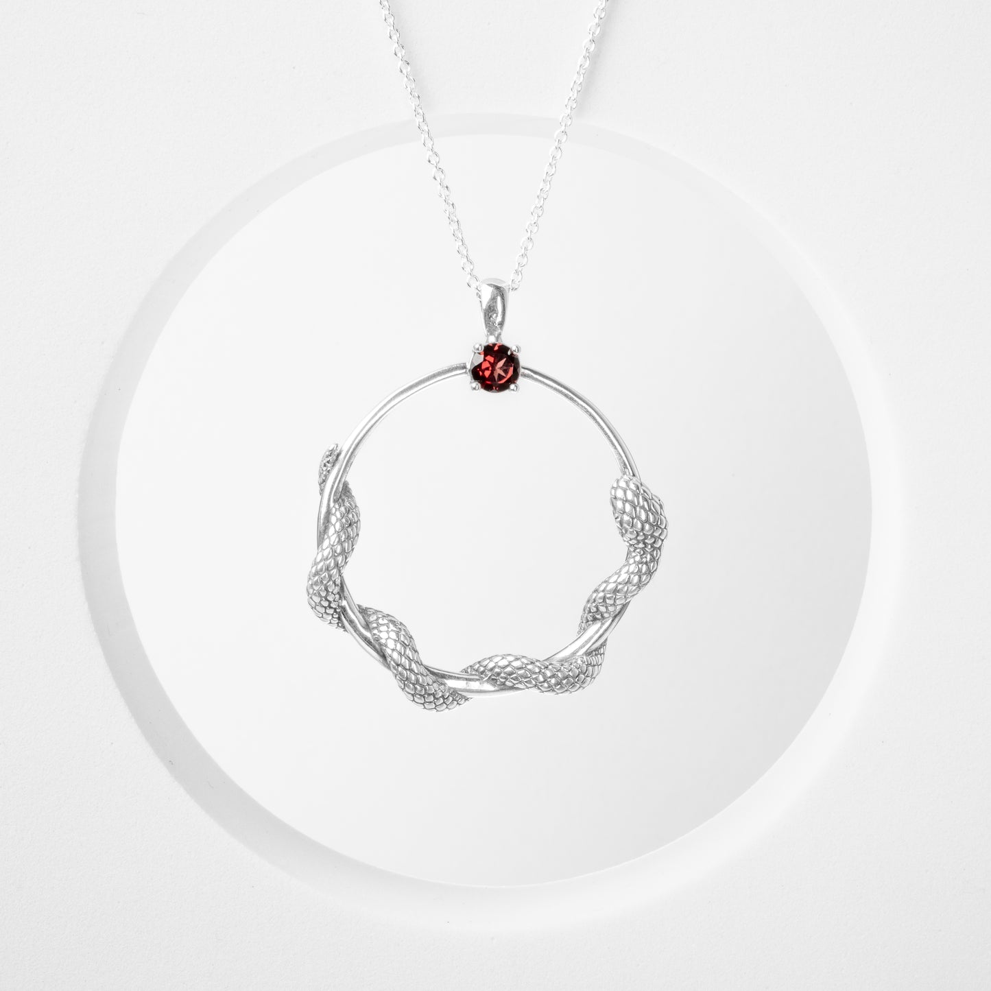 Pendente Circulus: cerchio in argento 925 brunito lucido con serpente stilizzato avvolto in basso e cabochon di onice nero incastonato nella parte superiore.