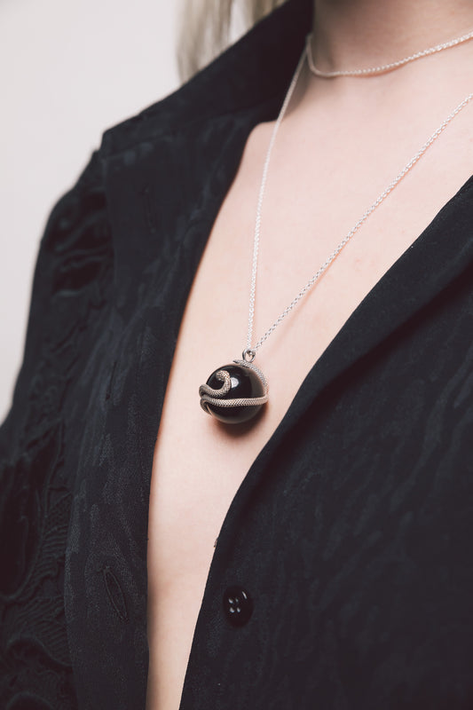 Primo piano del pendente Sphera con focus sul serpente in argento brunito che si avvolge attorno alla sfera in onice nero, evidenziando la texture metallo-pietra